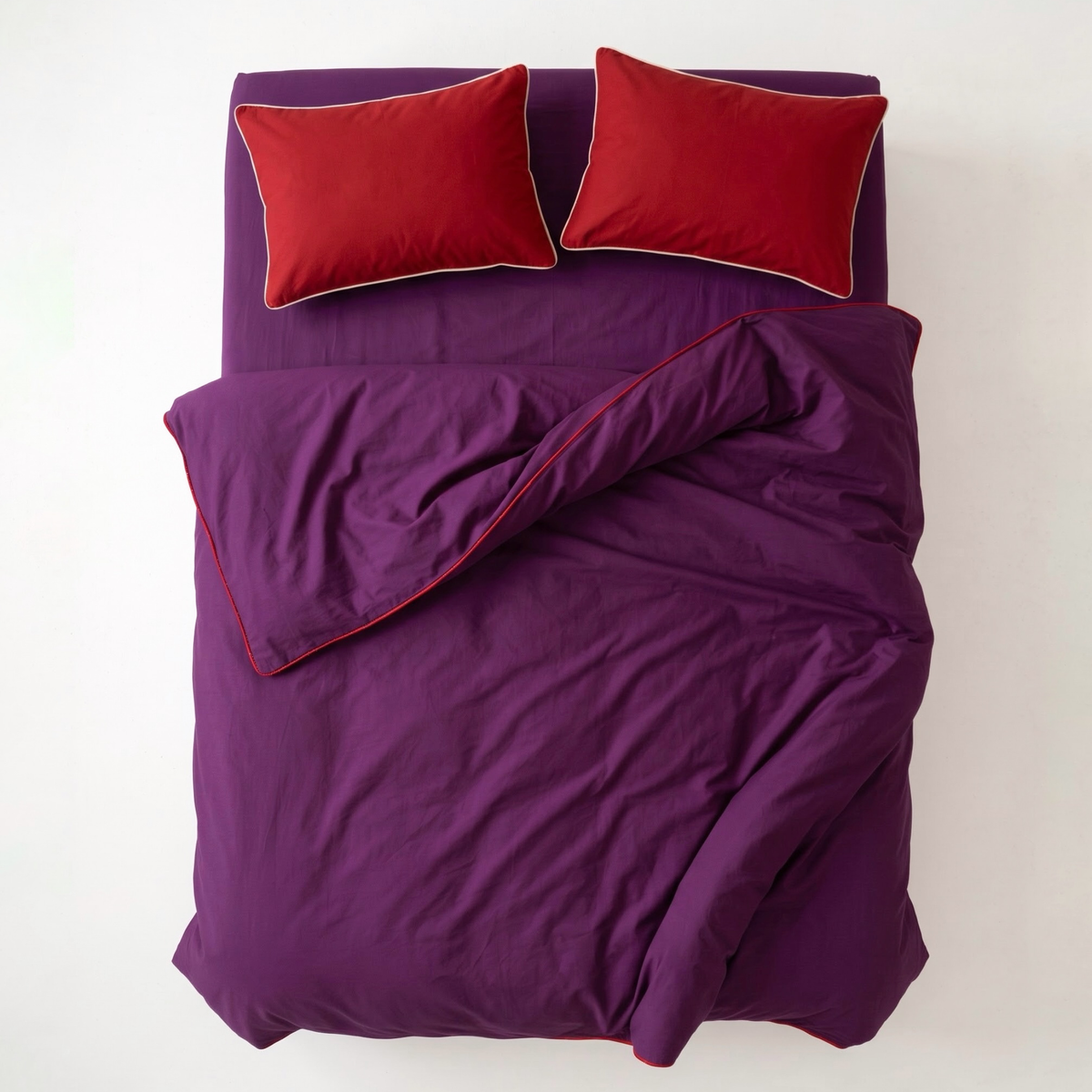 Purple bedding set with a duvet cover and two red pillows, photographed from above on a plain white background.