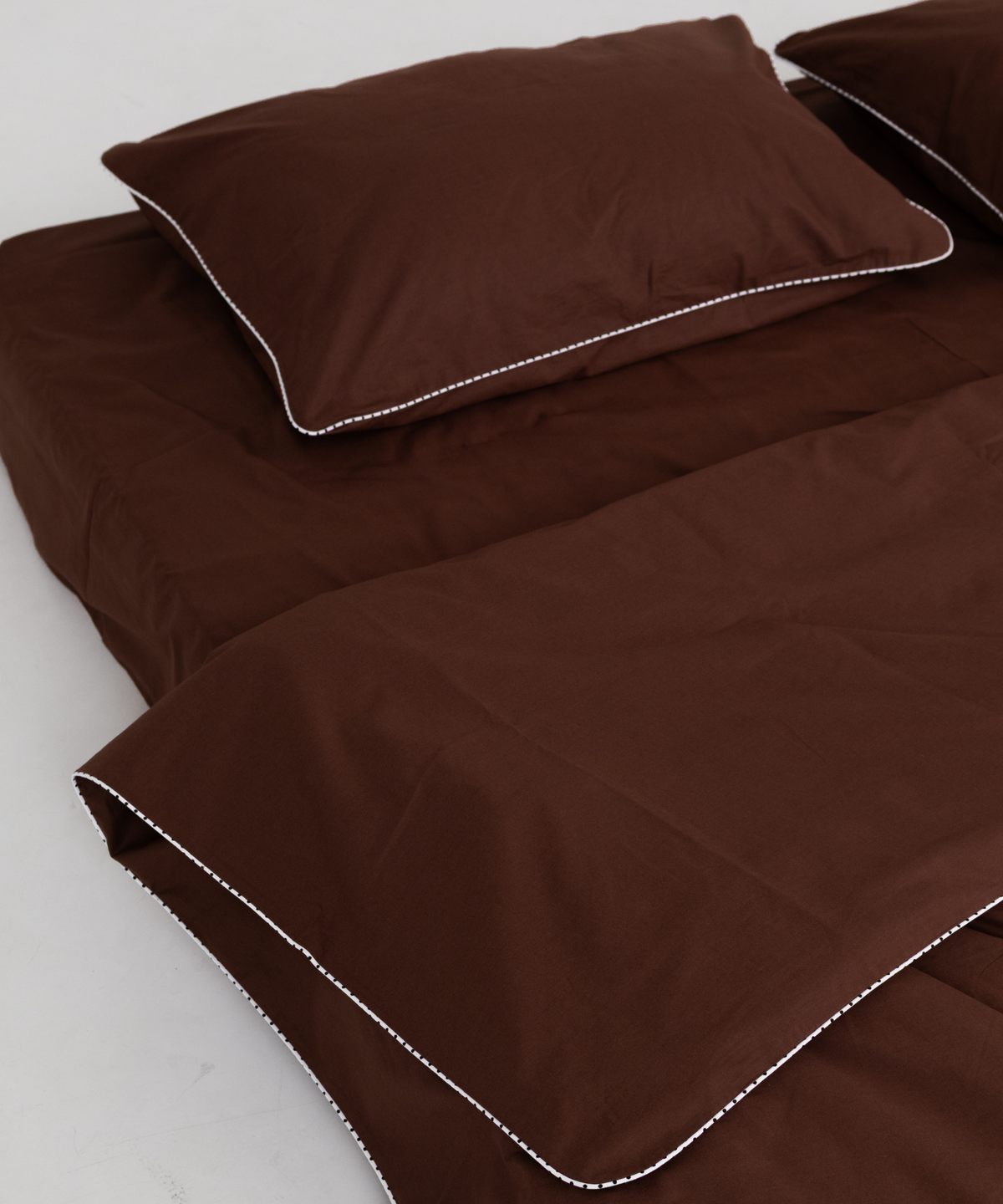 Brown bedding set including a duvet cover and pillowcases with contrasting white polka dot piping, displayed on a light gray background.