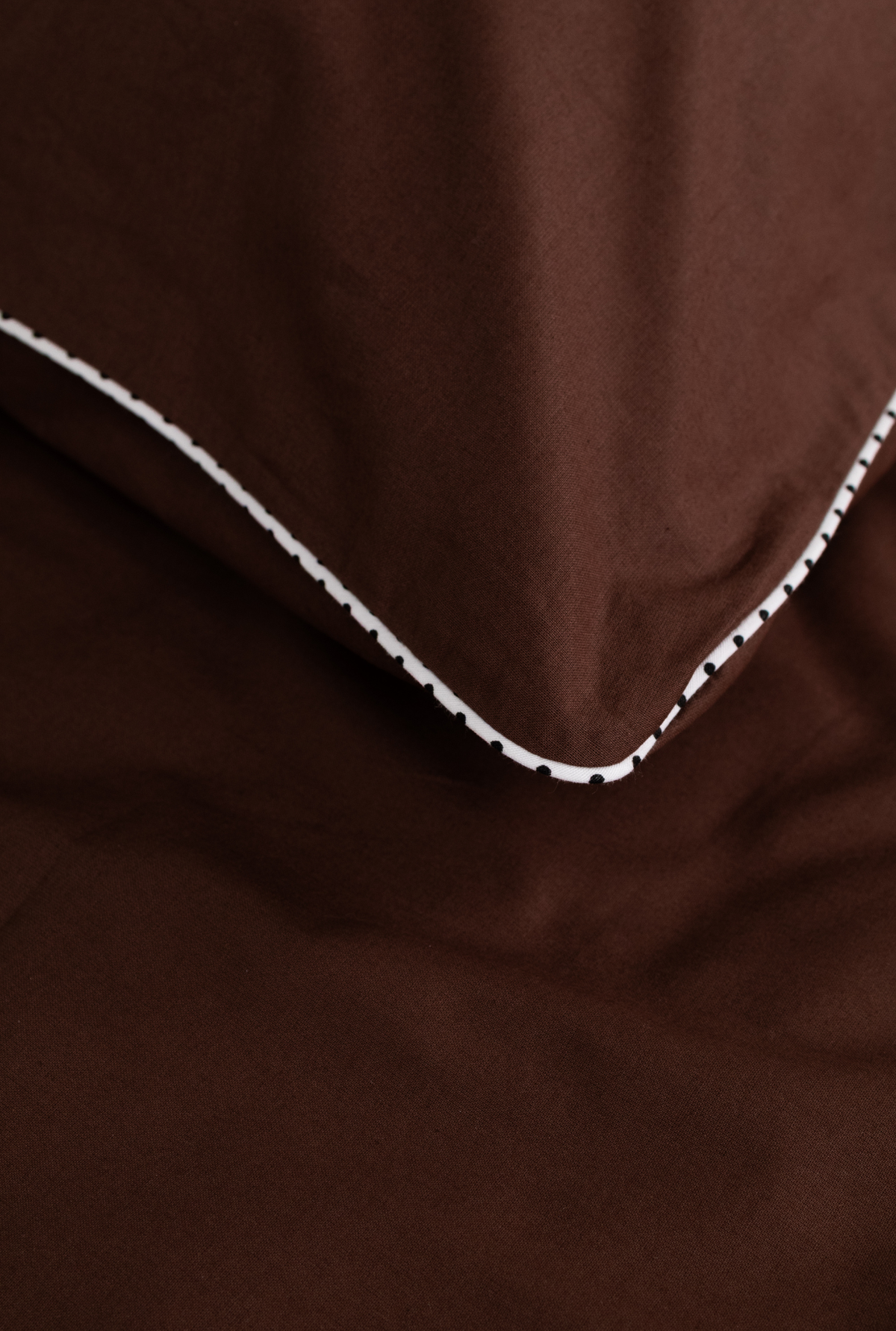 Close-up of a dark brown fabric item, likely bedding or a textile accessory, folded to show a white polka dot stitched edge.