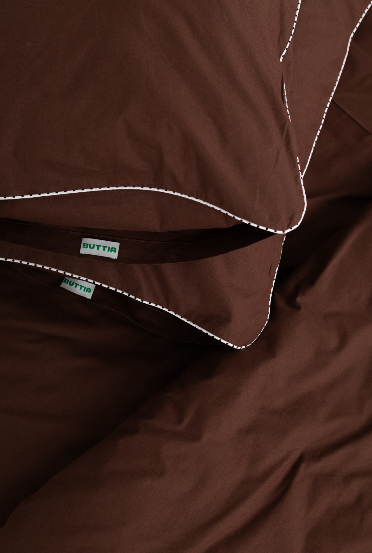 Close-up of a brown bedding set with white contrast stitching and visible BUTTIA brand labels on the inner band.