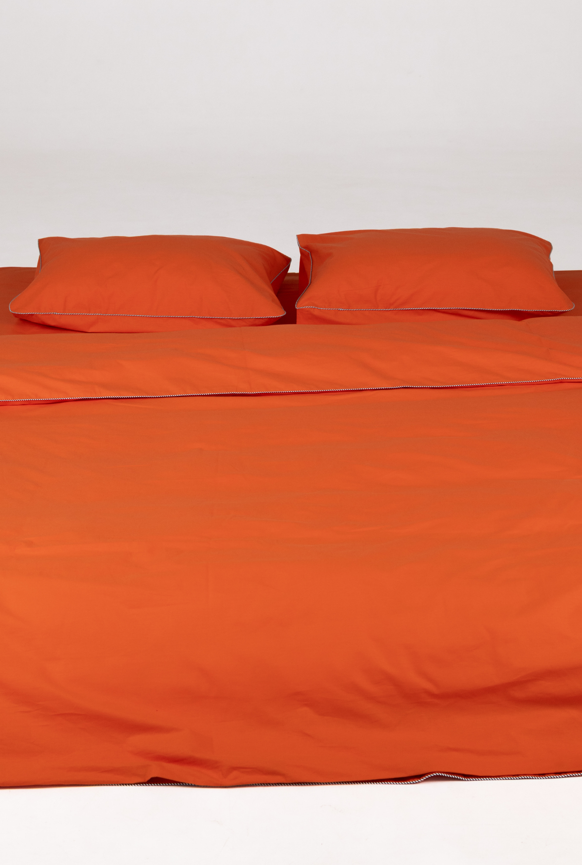 Bright orange bedding set including a duvet cover and two matching pillowcases, neatly arranged on a bed against a plain white background.