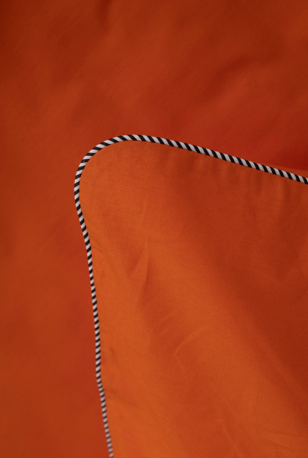 Close-up of an orange fabric surface with a black-and-white striped rope detail along the curved edge.