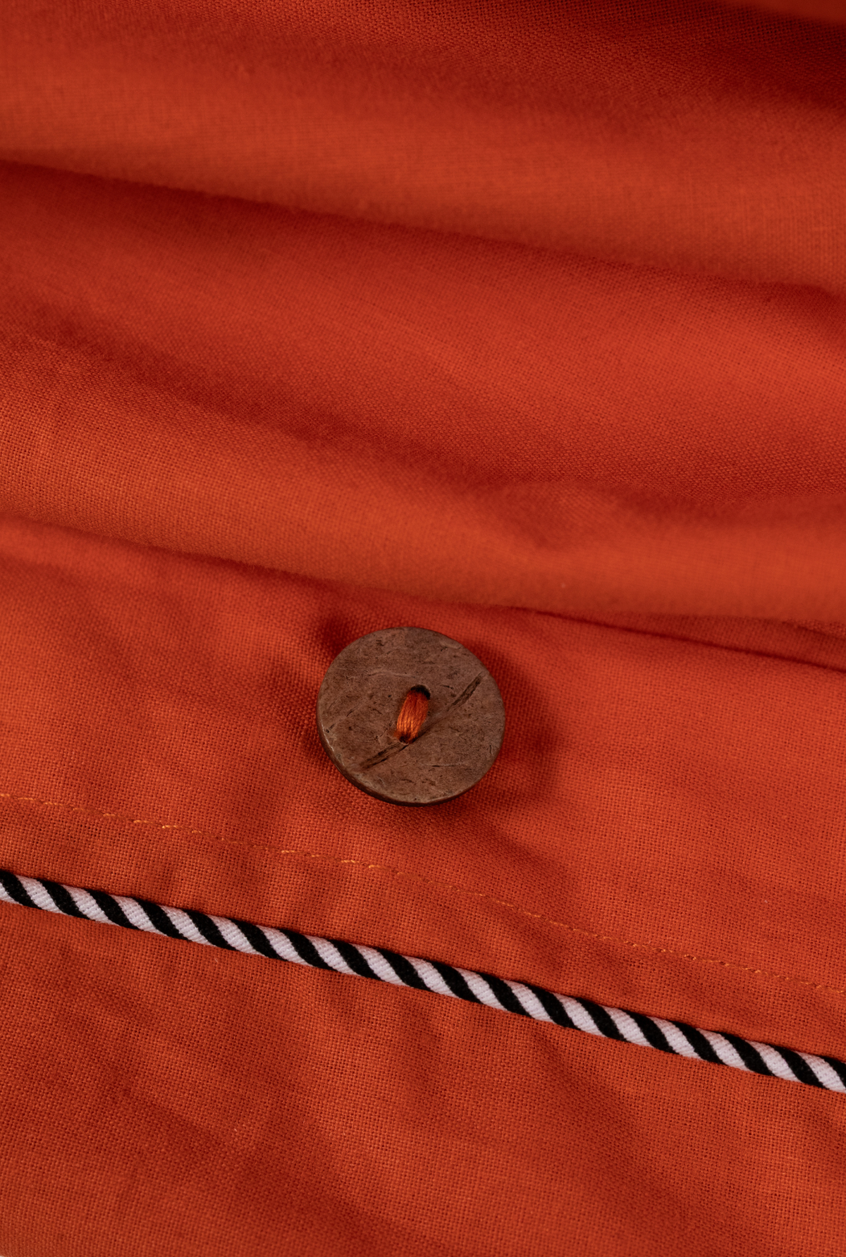 Close-up of an orange fabric surface with a round brown button and a black-and-white striped cord detail.