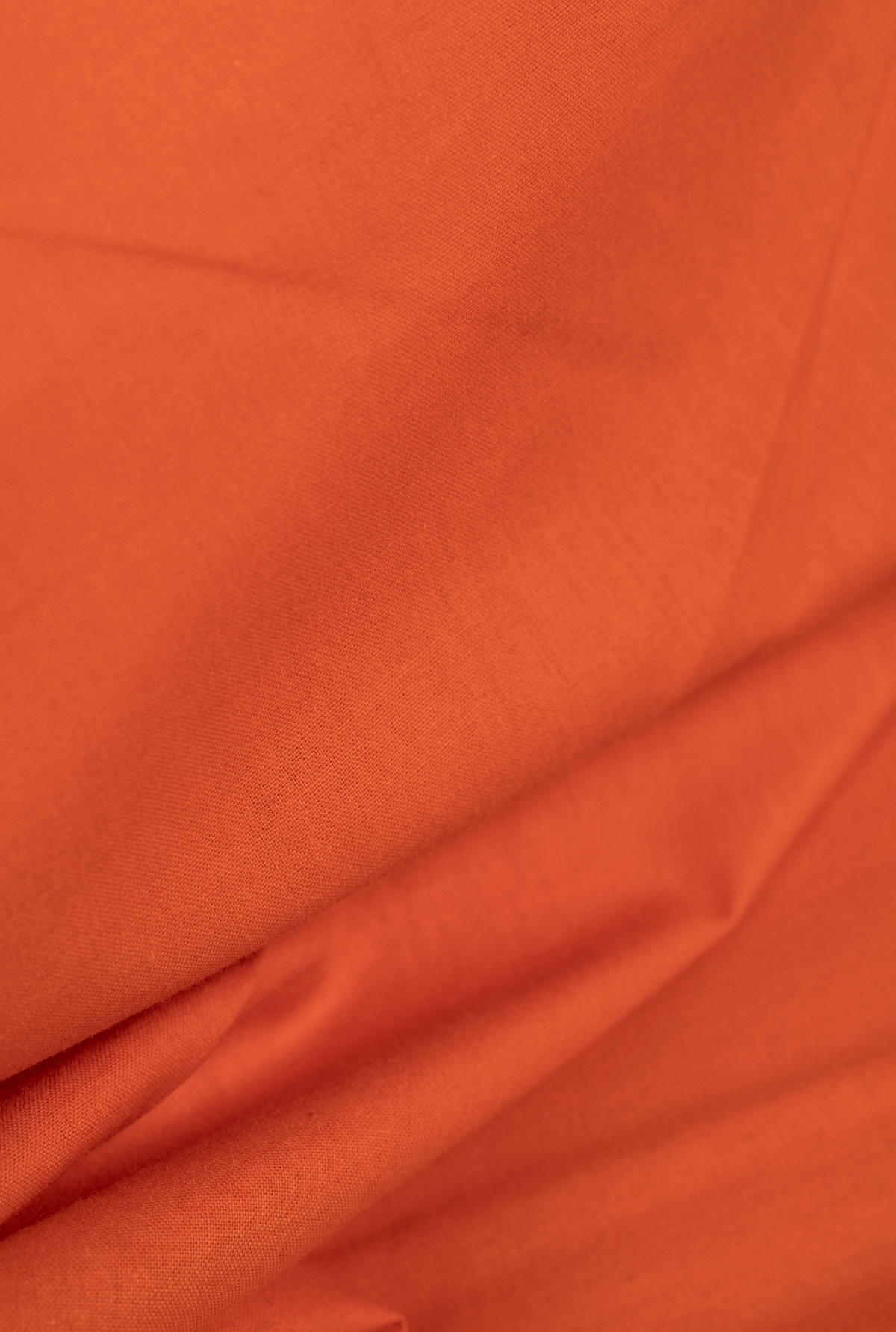 A close-up of draped orange fabric with soft folds and a smooth texture.