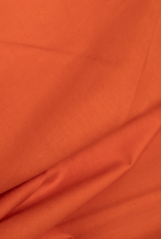 A close-up of draped orange fabric with soft folds and a smooth texture.