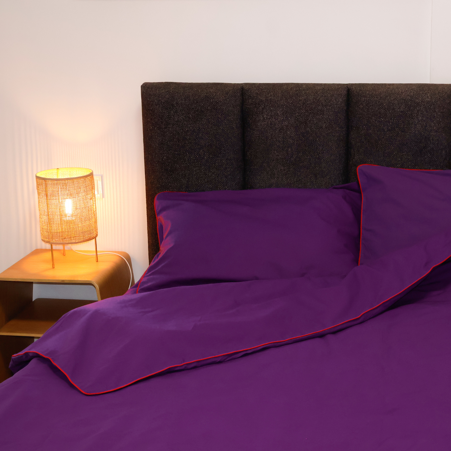 Natural purple bedding set by BUTTIA including a duvet cover and pillowcases with vibrant red piping.