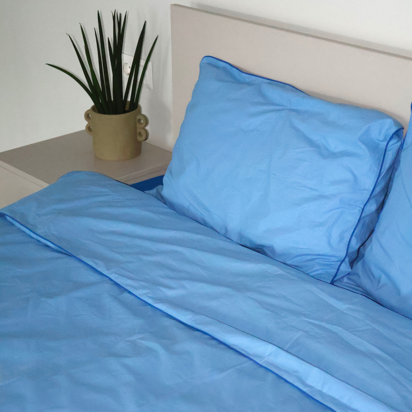 Natural blue bedding set by BUTTIA including a duvet cover and pillowcases with vibrant blue piping.