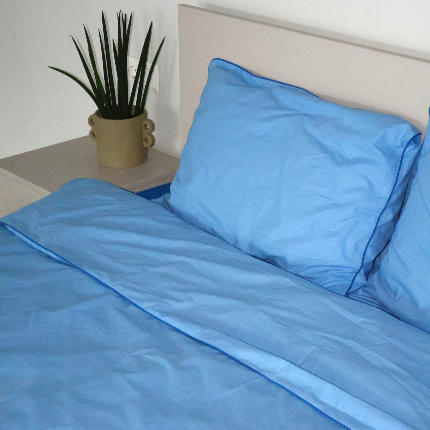 Natural blue bedding set by BUTTIA including a duvet cover and pillowcases with vibrant blue piping.
